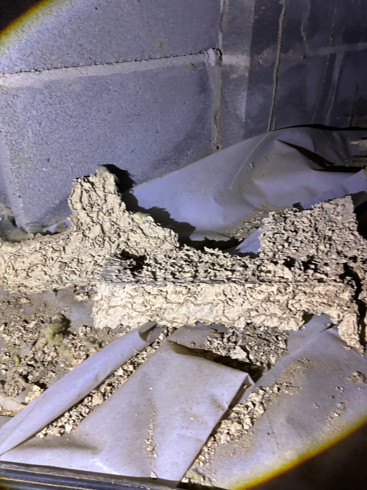 Raised termite mud tubes and soil debris across a crawl-space ground covering beside a block foundation.