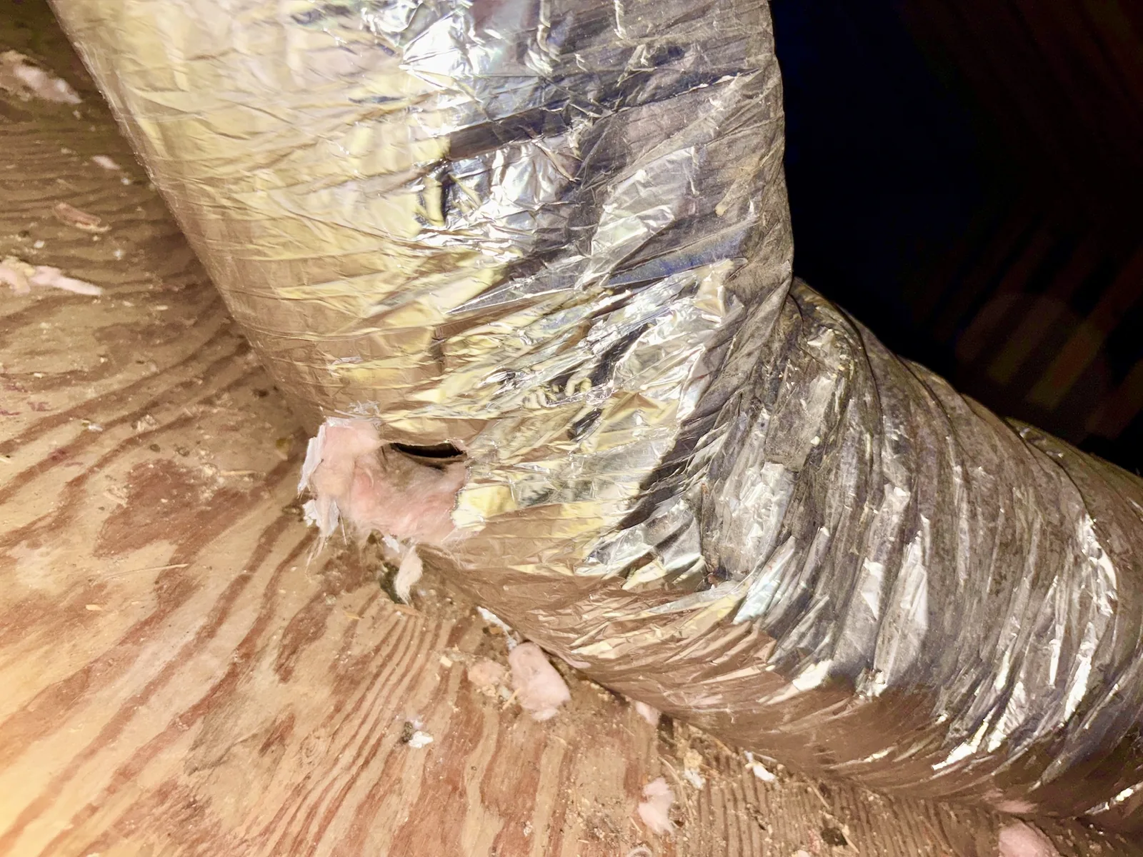 Flexible HVAC air duct with an opening chewed by rodents in a crawl space.