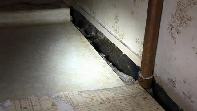 Inside a dim apartment kitchen cabinet, a gap runs along the seam where the counter meets the wall next to a plumbing pipe.