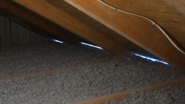 An attic interior with blown-in insulation between the joists, electrical cable stapled along a rafter, and a thin line of daylight showing at the eave.