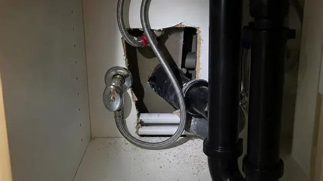 The inside of a condominium kitchen sink cabinet, where the drain trap and supply lines pass through the back wall toward the neighbouring unit.