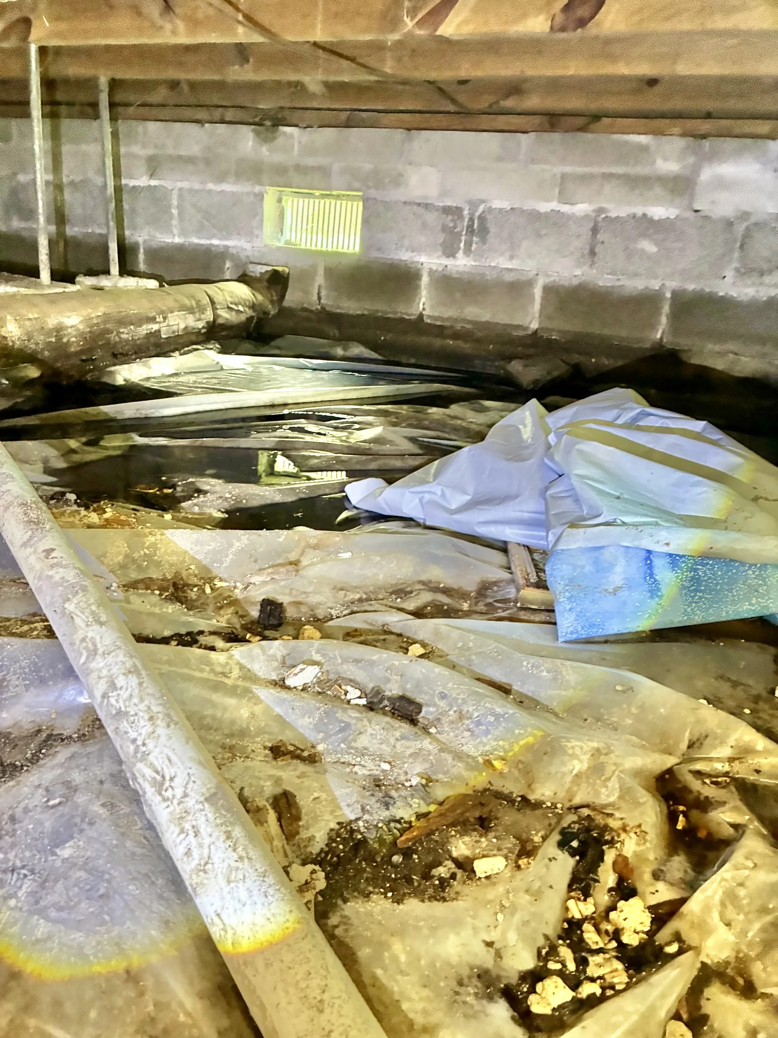 Owner-supplied photo of a wet crawl space with standing water, displaced ground cover, and debris before moisture-control work.