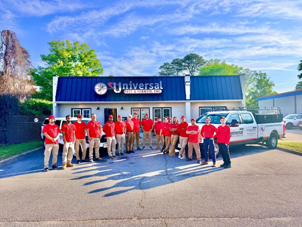 Universal Pest & Termite team standing outside company headquarters in Hampton Roads with technicians wearing red uniforms beside branded service trucks and the Universal Pest & Termite office building.