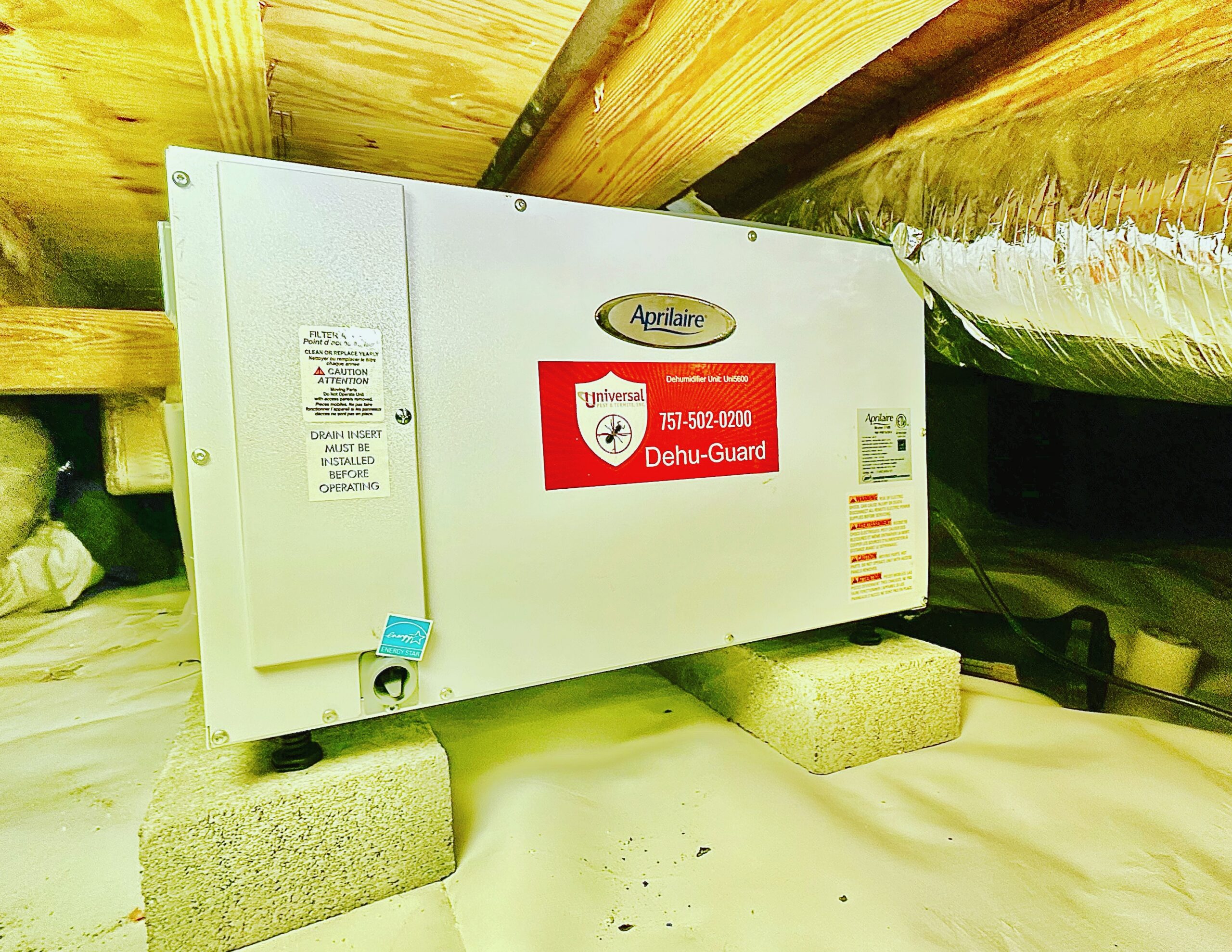 Professional Aprilaire crawlspace dehumidifier with a branded Universal Pest & Termite Dehu-Guard shield installed on concrete blocks over a clean vapor barrier in a Woodard Mill home in Chesapeake, VA